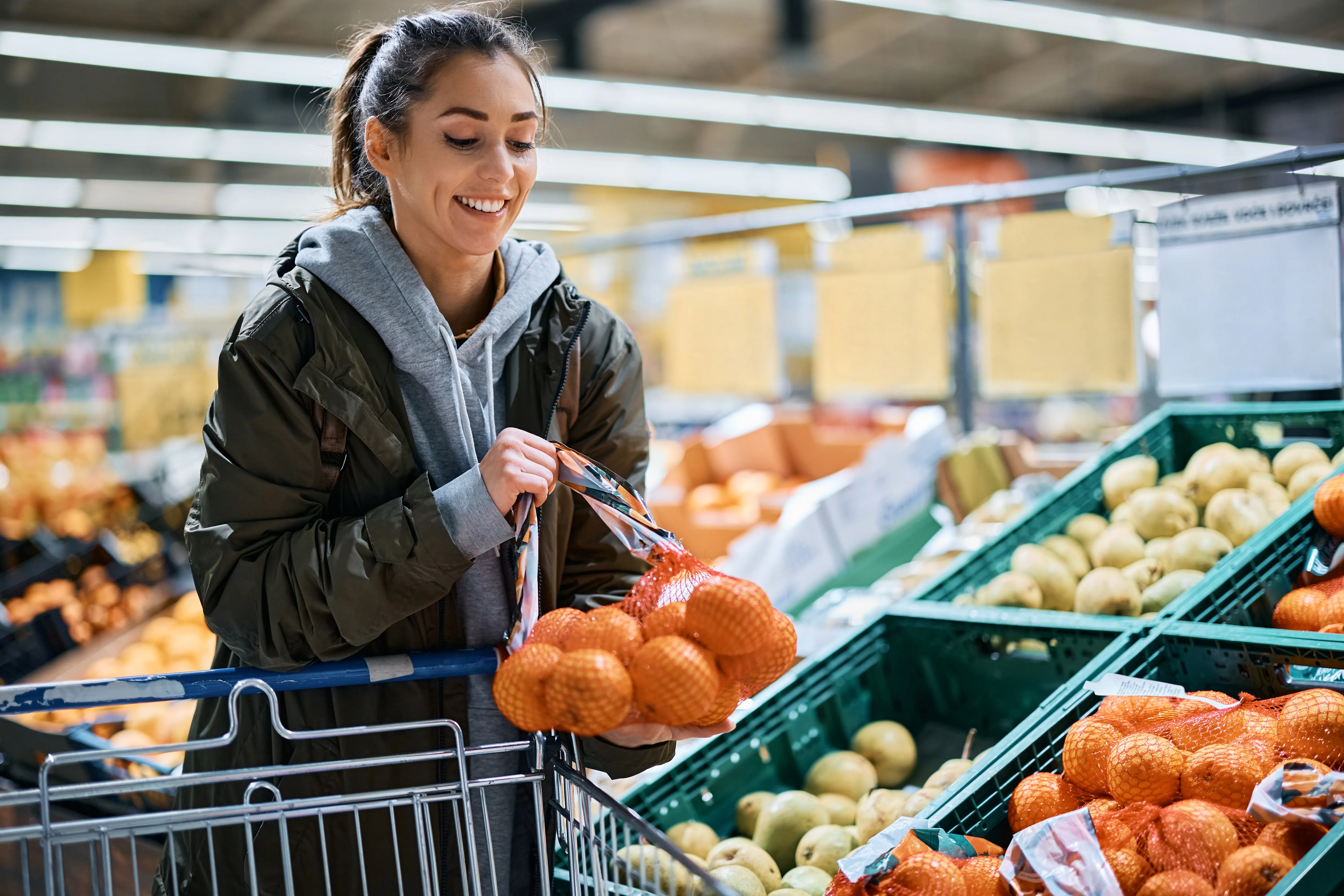 Vrouw die fruit kiest in de supermarkt met een winkelwagen
